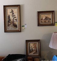 Three framed landscape paintings hanging on wall above couch and lamp
