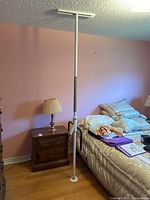 Full view of the adjustable bed assist pole installed next to bed and nightstand, showing the pole’s full height and ceiling and floor contact points.