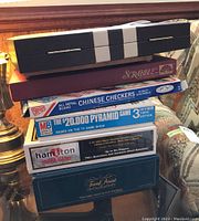 Stack of six board game boxes on a wooden surface, showing titles and colors of each game box to identify contents.
