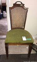 Front view of wood chair showing caned backrest, upholstered green seat, and wood legs.