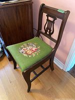 Side angle view of the wooden chair showing needlepoint floral upholstered seat and curved backrest with some wear on finish.