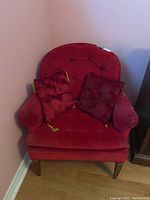 Front view of red button tufted upholstered armchair with two tasseled cushions placed on seat, showing minor wear and condition of tassels.