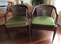Full view of two wooden tub style chairs with caned backs and green cushions placed on a wooden floor, showing details of armrests and frame design.