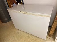 White Kenmore chest freezer positioned on a tiled floor with visible wear and tear on the top and front surfaces.