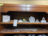 Two wooden shelves containing crystal figurines, a boxed glass paperweight, a wood clock, Wolf Original figurine, and various miniatures