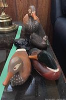 Group shot of four wooden duck decoys and one loon decoy on a glass table