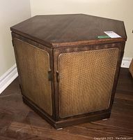 Hexagonal wooden end table with woven cane panel doors, shown closed, highlighting the shape and texture of the doors and wood finish.