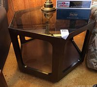 Hexagonal dark wooden end table with glass top and open storage shelf underneath, angled side view showing construction and shape.