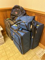 Photo showing stacked luggage sets with blue Roots suitcases and duffel bag, American Tourister gym bag seen on top