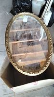 Oval mirror inside a box, frame gold with raised floral decorative pattern, glass surface dusty with backing loose.