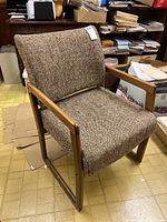 Side angle view of the upholstered office chair showing wood arms and legs with brown textured fabric and some missing wood plugs.