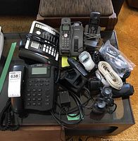 Photo showing multiple corded and cordless phones, multiple cables, and phone accessories on a glass table.