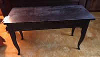 Wood piano bench with scratches on the seat surface and curved legs.