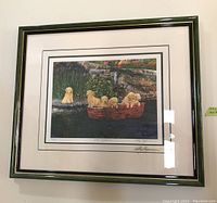 Framed print showing five yellow Labrador Retriever puppies, four in a red boat and one on a rock, with garden and stone wall background.