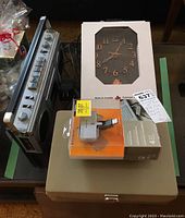 Items including Mona MS-1000 radio, clock in box, rotating USB hub, calculator on top of beige metal cash box.