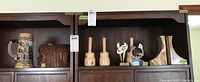 Shelf display showing several decorative items including a ceramic stein, carved wood bookends, onyx stone bookends, and three small trophies.