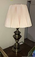 Full view of the brass style table lamp showing the base and the pleated beige shade.