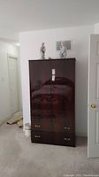 Front view of dark faux wood armoire standing in a carpeted room, showing two doors and two drawers with brass handles
