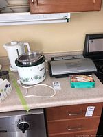 Countertop with four appliances: white electric kettle, floral crock pot slow cooker, silver vacuum sealer, and boxed crepe maker trio.