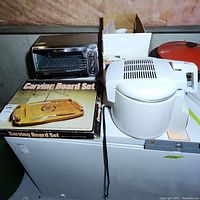 Photo showing Hamilton Beach toaster oven, wooden carving board set in original box, and Moulinex deep fryer with Micro-Filter Safety on top of a freezer chest.