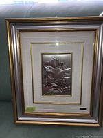 Full view of framed silver relief artwork depicting mountain village and mountains.