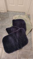 Four bathroom mats arranged on tiled floor, three dark blue and one light green.