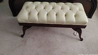 Full view of carved wood bench with tufted cream leather seat showing overall condition and design.