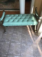 Front view showing tufted mint green leather seat with decorative metal leg supports.