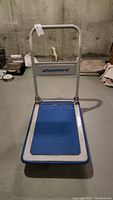 Front view of the Shepherd folding push cart showing brand name and blue textured platform surface on metal frame.