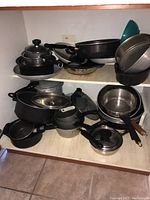 Full cupboard shelf with various pots, pans, lids stacked and overlapping, showing breadth of collection.