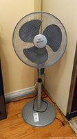 Full view of Wind Chaser standing oscillating fan with three dark blades inside a metal mesh guard, showing base, pole, and control panel.