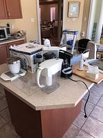 Photo showing various kitchen items on a kitchen counter including the white water filter pitcher, Black and Decker blender, clear plastic organizer, Black and Decker electric can opener, and KitchenAid black dish rack.