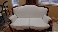 Full front view of the white upholstered love seat showing carved wood frame and cushions.