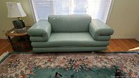 Front view of the light blue/green leather love seat showing rounded armrests and smooth upholstery