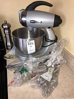 Sunbeam Heritage Series Mixmaster Legacy Edition silver stand mixer with black handle and stainless steel bowl. Several mixer attachments wrapped in plastic in front of the mixer, a stainless steel pepper mill beside it.