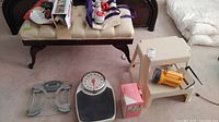 Overview photo of the lot showing all items including two scales, jewelry cleaner box, massager, flashlight, and step stool on carpet.