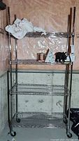 Metal shelving unit on wheels with four wire shelves in a basement corner, holding miscellaneous items not included.