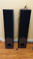 Two Pioneer S-H551F-K tower speakers standing side by side with wiring tangled on top of one speaker.