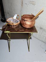 Folding table holding a woven basket, copper pot, and wooden utensils in basement setting