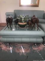 Front view of leather coffee table with green upholstery showing beveled glass inset and decorative horse figurines on top.