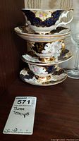 Three stacked teacups with matching saucers showing detailed gilding and floral patterns.