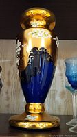 Front view of Bohemian hand painted glass vase showing cobalt blue and gold with white floral details.