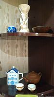 Photo of shelf showing the porcelain vase, alabaster figurine, small wooden bowl, clay teapot with two sake cups, and miniature Delft teapot house