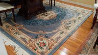 Full view of the vintage wool rug showing the floral pattern and border under dining furniture on hardwood floor.