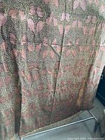 Full view of fringed throw with pink leaf pattern against textured green and dark background.