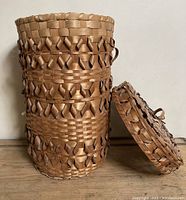 Tall cylindrical vintage MicMac basket with separate lid leaning beside it. Basket shows detailed patterned weave and side handles.
