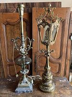 Two tall vintage table lamps showing one with ornate brass and glass design and the other with a brass lantern-style construction