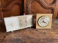 Wide view showing both vintage clocks on wooden surface with carved wood background.