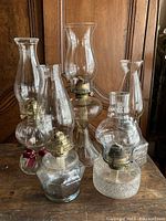 Overall view of five vintage glass oil lamps on wooden surface, showing variety in shape and size.