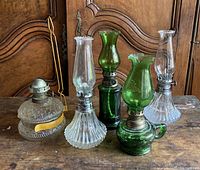 Full view of five oil lamps on wooden table showing clear and green glass types